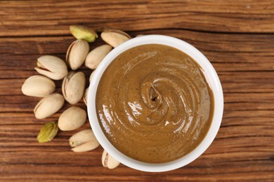 Delicious nut butter in bowl and pistachios on wooden table, top view