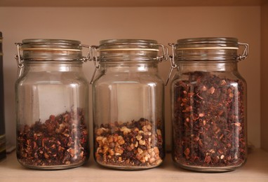 Different types of tea with dried fruit slices in glass jars on wooden shelf