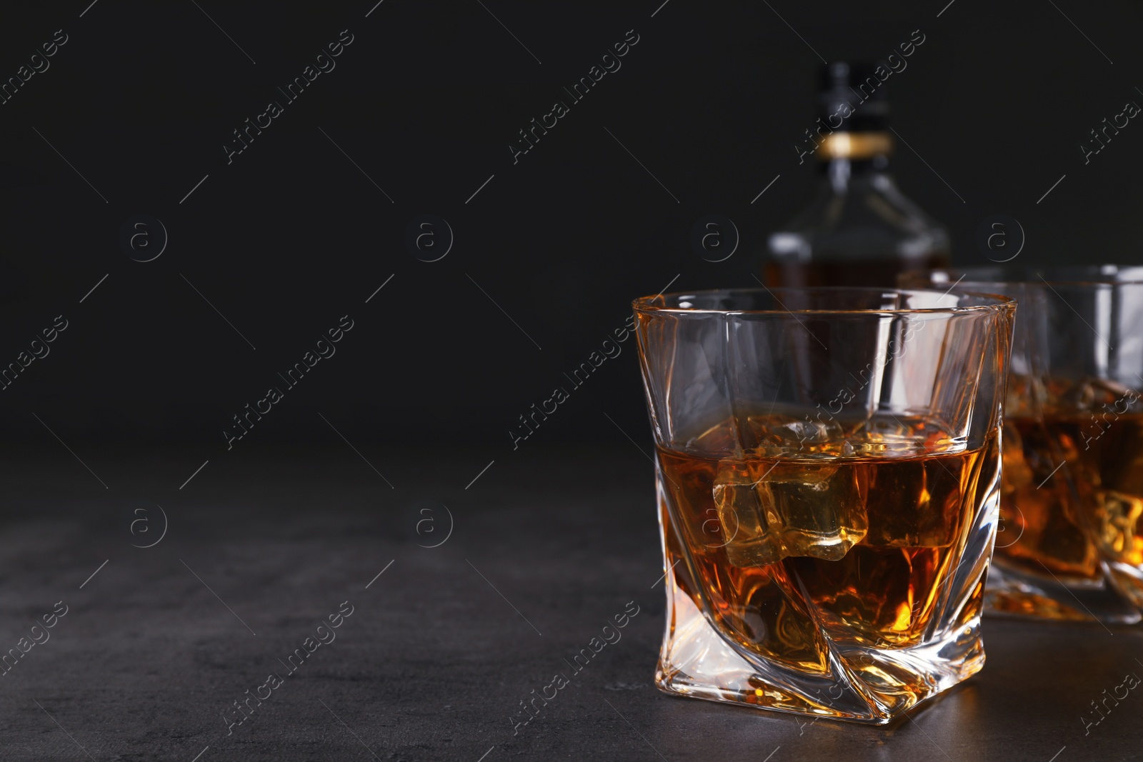 Photo of Golden whiskey in glass with ice cubes on table. Space for text