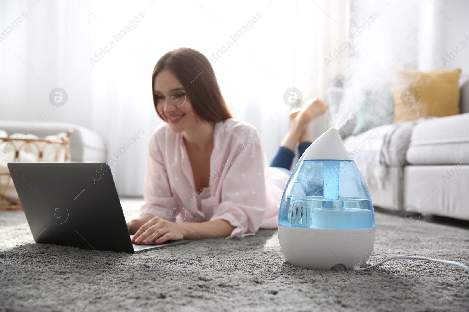 Photo of Woman with laptop near modern air humidifier at home