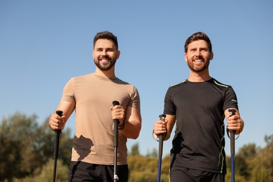 Happy men practicing Nordic walking with poles outdoors on sunny day