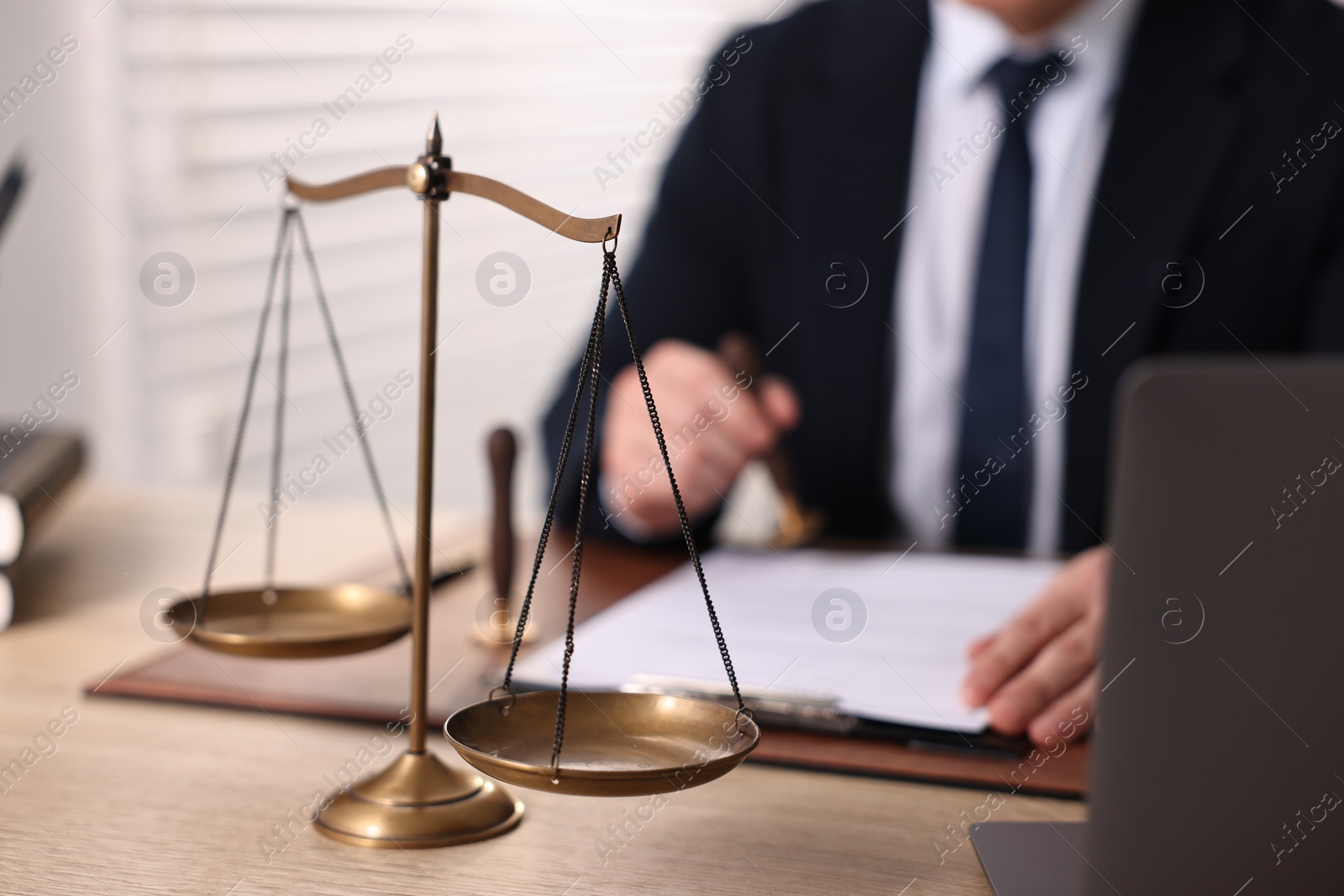 Photo of Notary stamping document at wooden table in office, focus on scales of justice