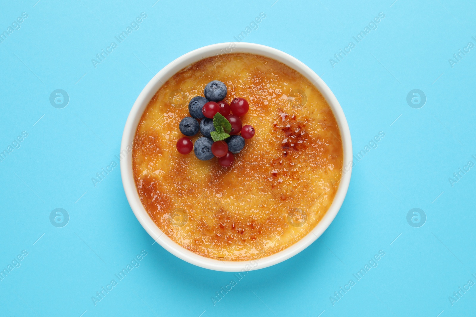 Photo of Delicious creme brulee with fresh berries and mint on light blue background, top view