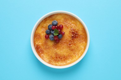 Delicious creme brulee with fresh berries and mint on light blue background, top view