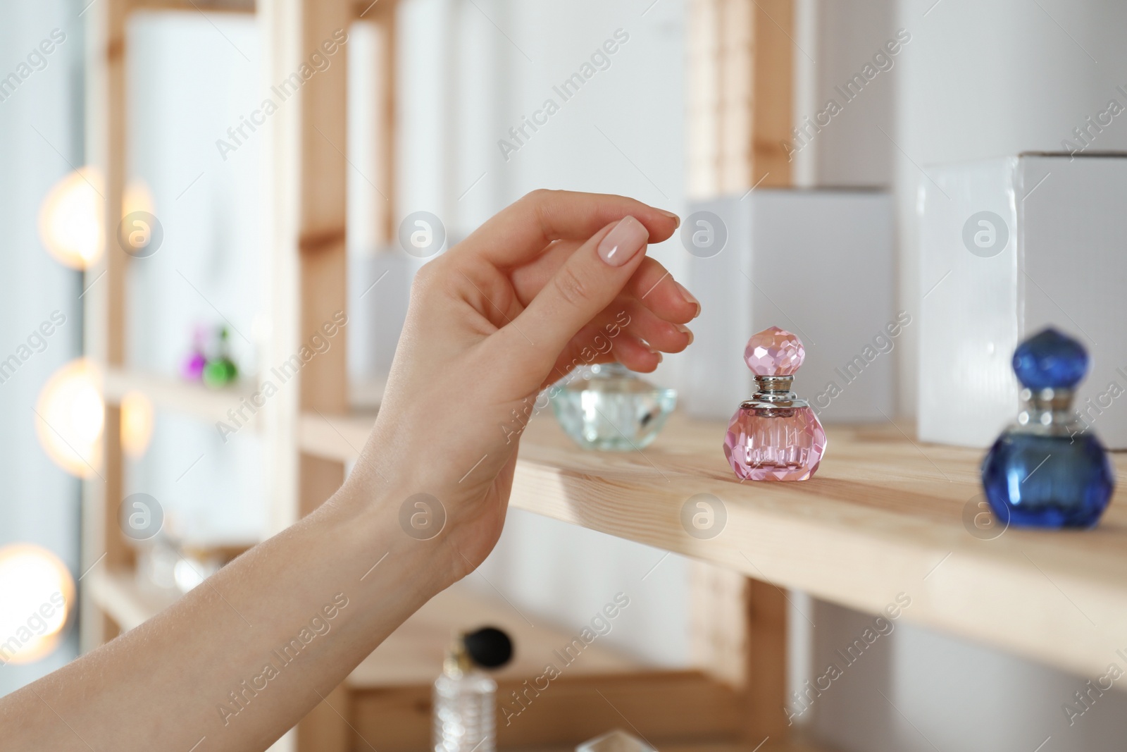 Photo of Woman taking bottle of perfume from wooden shelf indoors, closeup