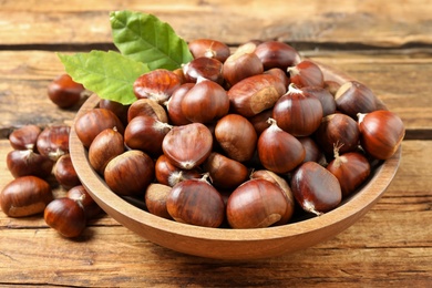 Photo of Fresh sweet edible chestnuts in bowl on wooden table