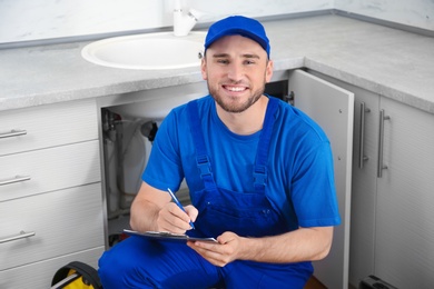 Photo of Professional plumber in uniform with clipboard near kitchen sink