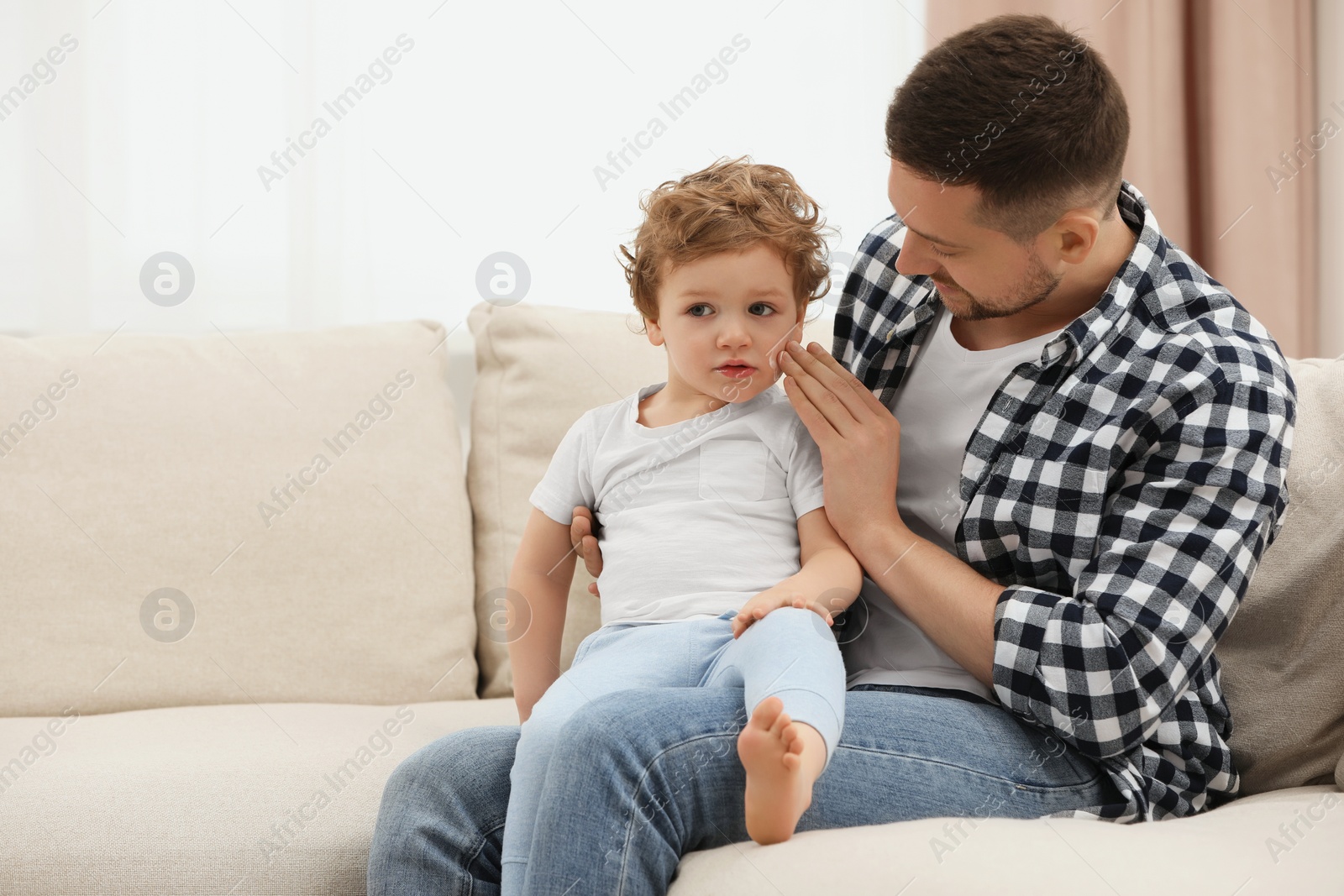 Photo of Father applying ointment onto his son`s cheek on sofa at home. Space for text