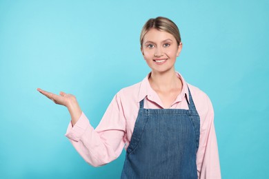 Beautiful young woman in denim apron on light blue background