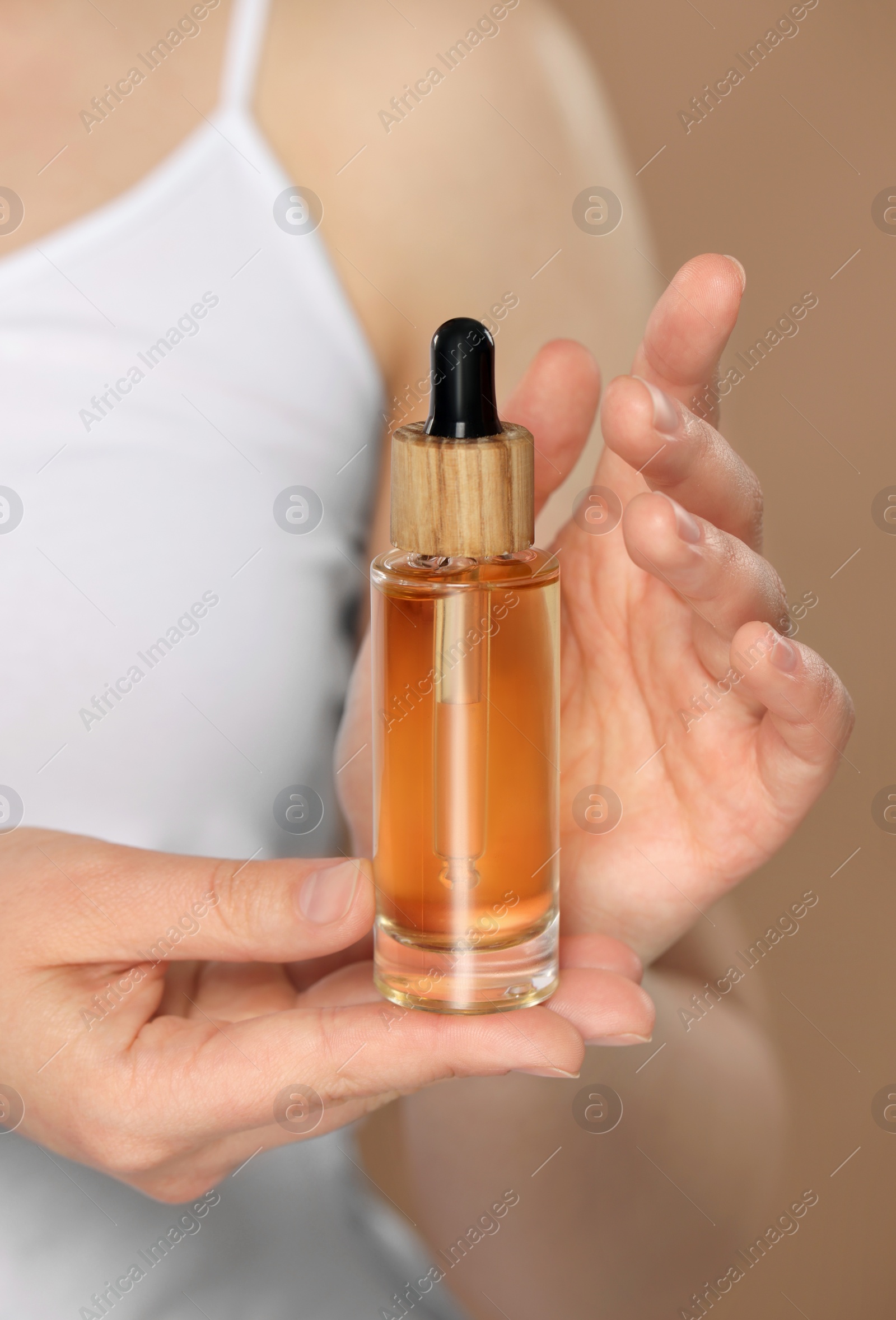 Photo of Woman holding bottle of essential oil on brown background, closeup