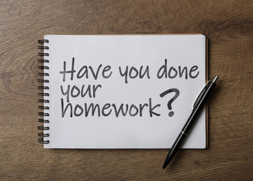 Image of Pen and stylish notebook with phrase HAVE YOU DONE YOUR HOMEWORK? on wooden table, top view