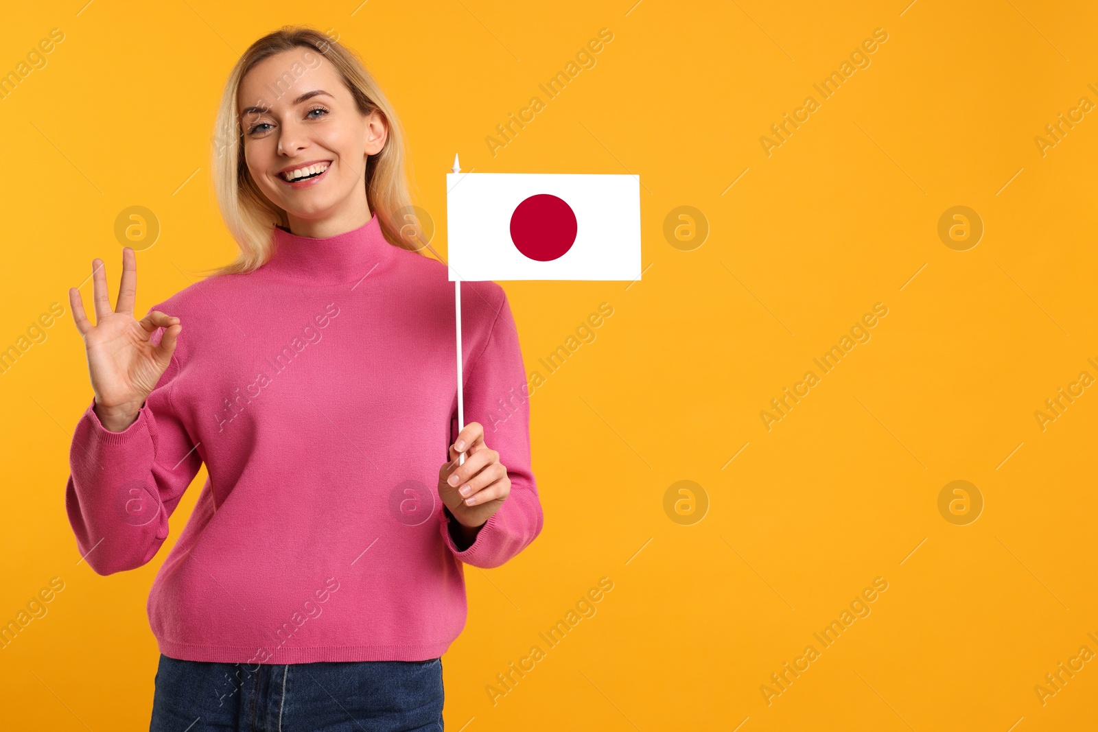 Image of Happy young woman with flag of Japan showing OK gesture on yellow background