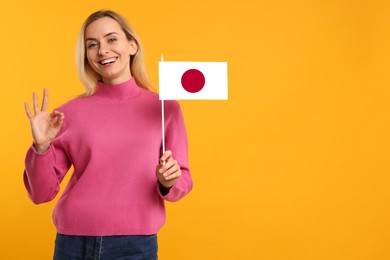 Happy young woman with flag of Japan showing OK gesture on yellow background