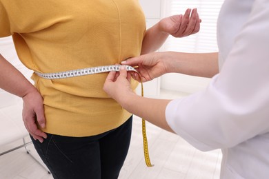 Photo of Nutritionist measuring overweight woman's waist with tape in clinic, closeup