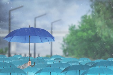 Image of Person holding umbrella over other under heavy rain outdoors 