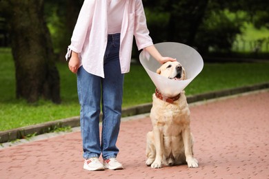 Photo of Woman petting her adorable Labrador Retriever dog in Elizabethan collar outdoors, closeup