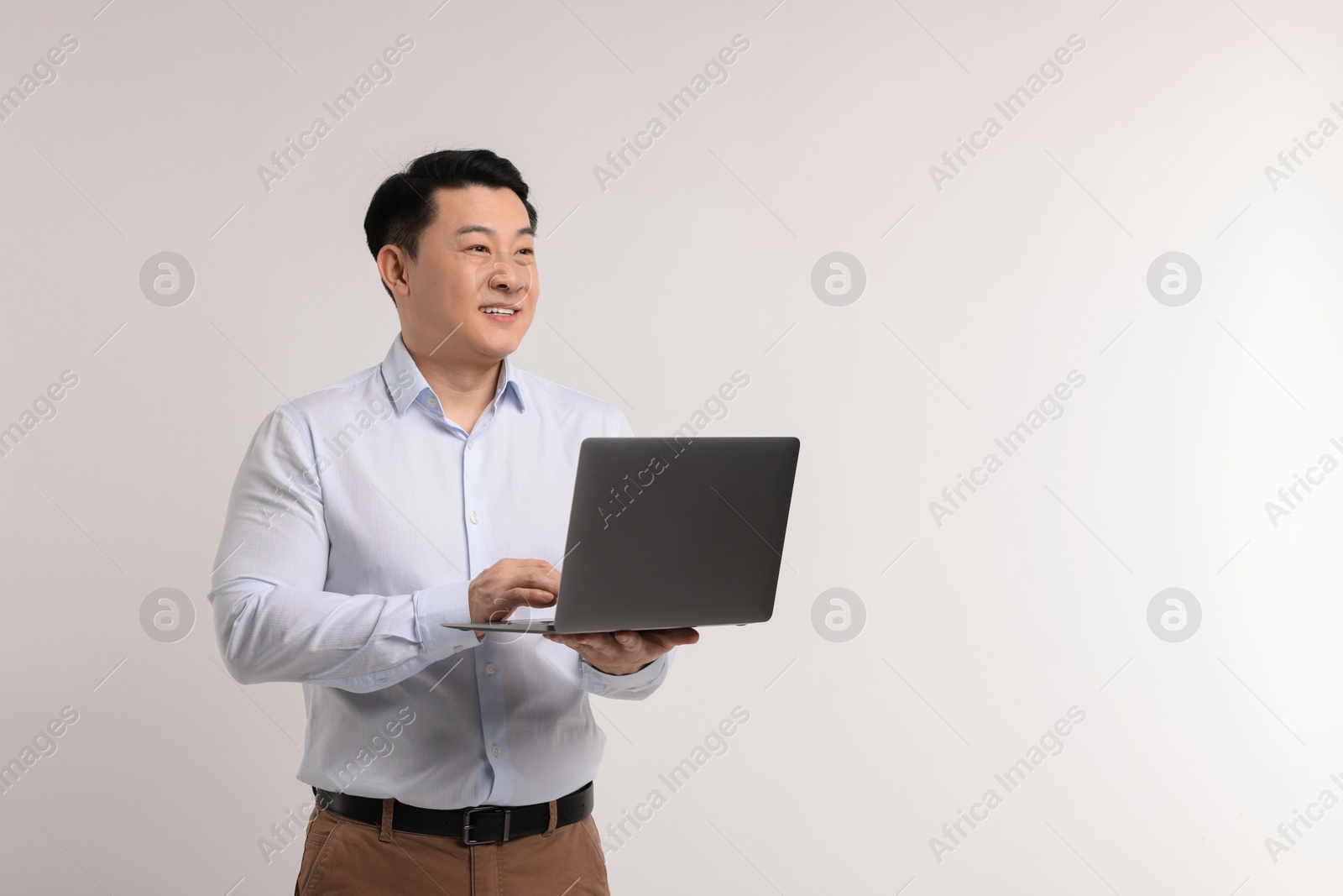 Photo of Portrait of happy man with laptop on light background. Space for text
