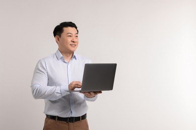Portrait of happy man with laptop on light background. Space for text
