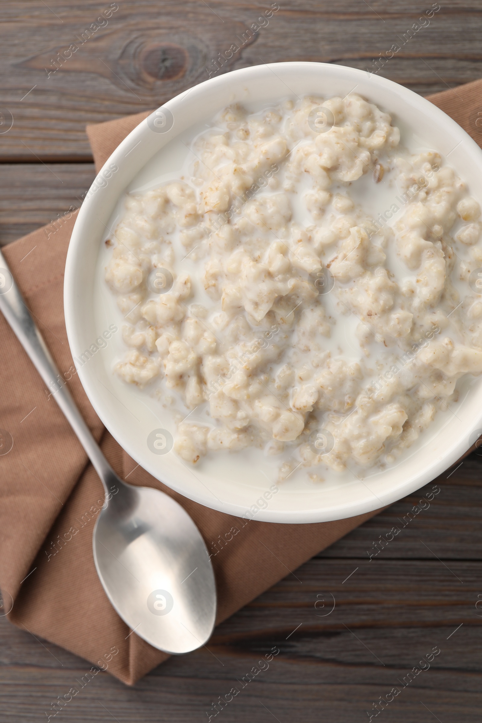 Photo of Tasty boiled oatmeal in bowl and spoon on wooden table, top view