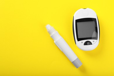 Digital glucometer and lancet pen on yellow background, flat lay with space for text. Diabetes control