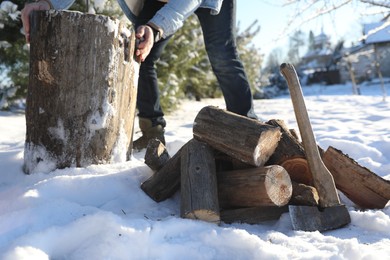 Photo of Man preparing stump for chopping outdoors, closeup. Axe and pile of logs on snow, selective focus
