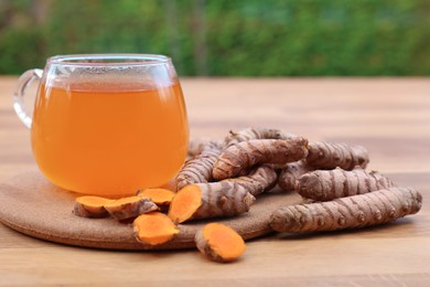 Glass cup of hot tea and fresh turmeric roots on wooden table