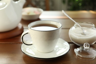 Photo of Cup of aromatic tea and sugar on wooden table, closeup