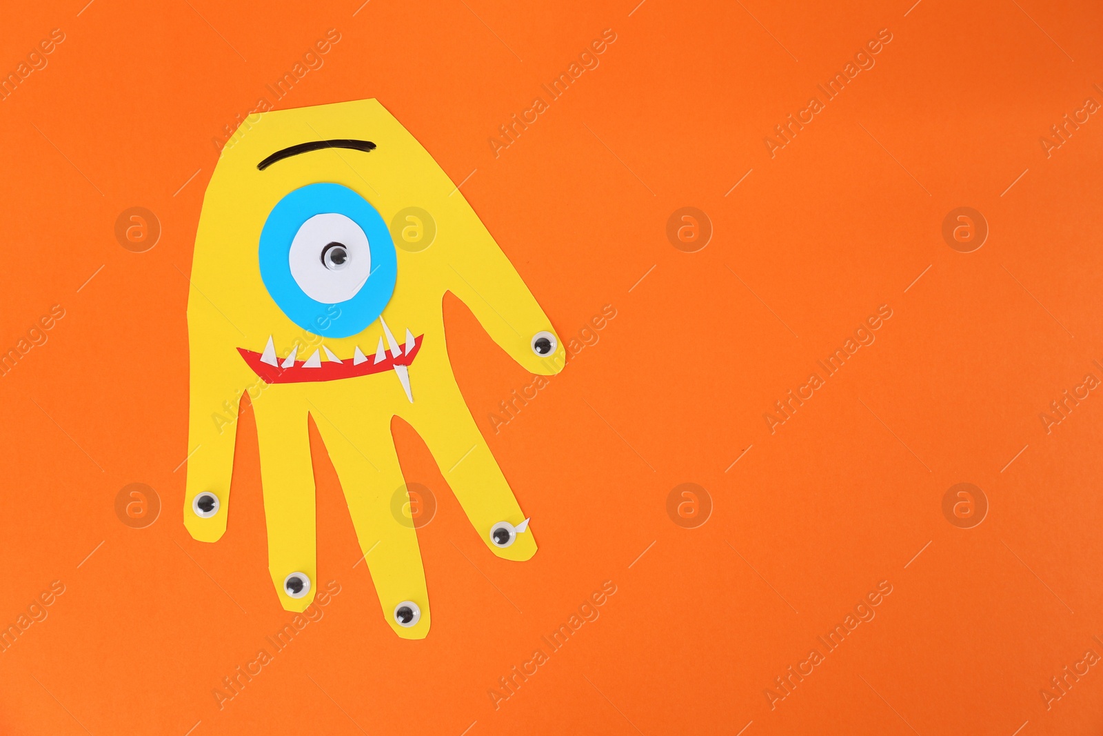Photo of Funny yellow hand shaped monster on orange background, top view with space for text. Halloween decoration