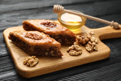 Photo of Delicious sweet baklava with walnuts and honey on black wooden table, closeup