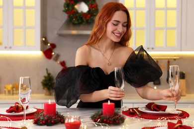 Beautiful young woman setting table for Christmas celebration in kitchen