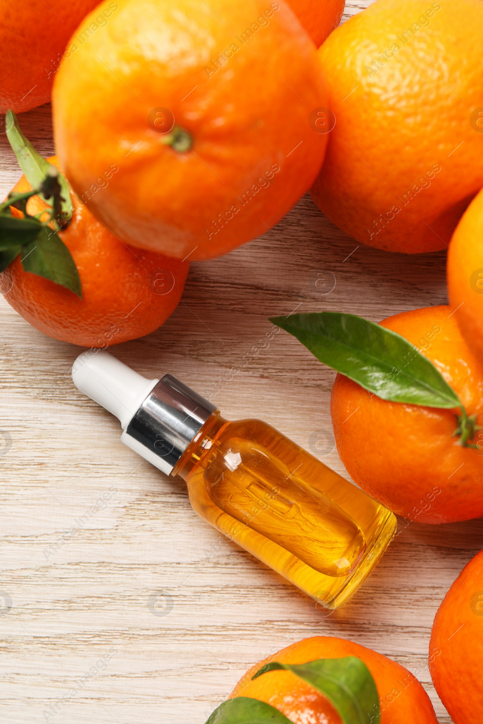 Photo of Bottle of tangerine essential oil and fresh fruits on white wooden table, flat lay