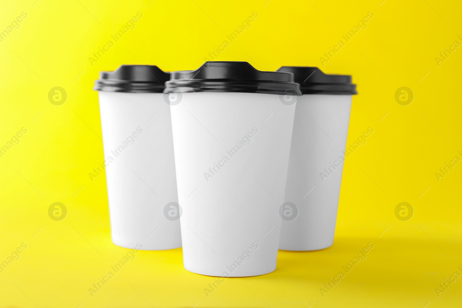 Photo of Paper cups with black lids on yellow background. Coffee to go