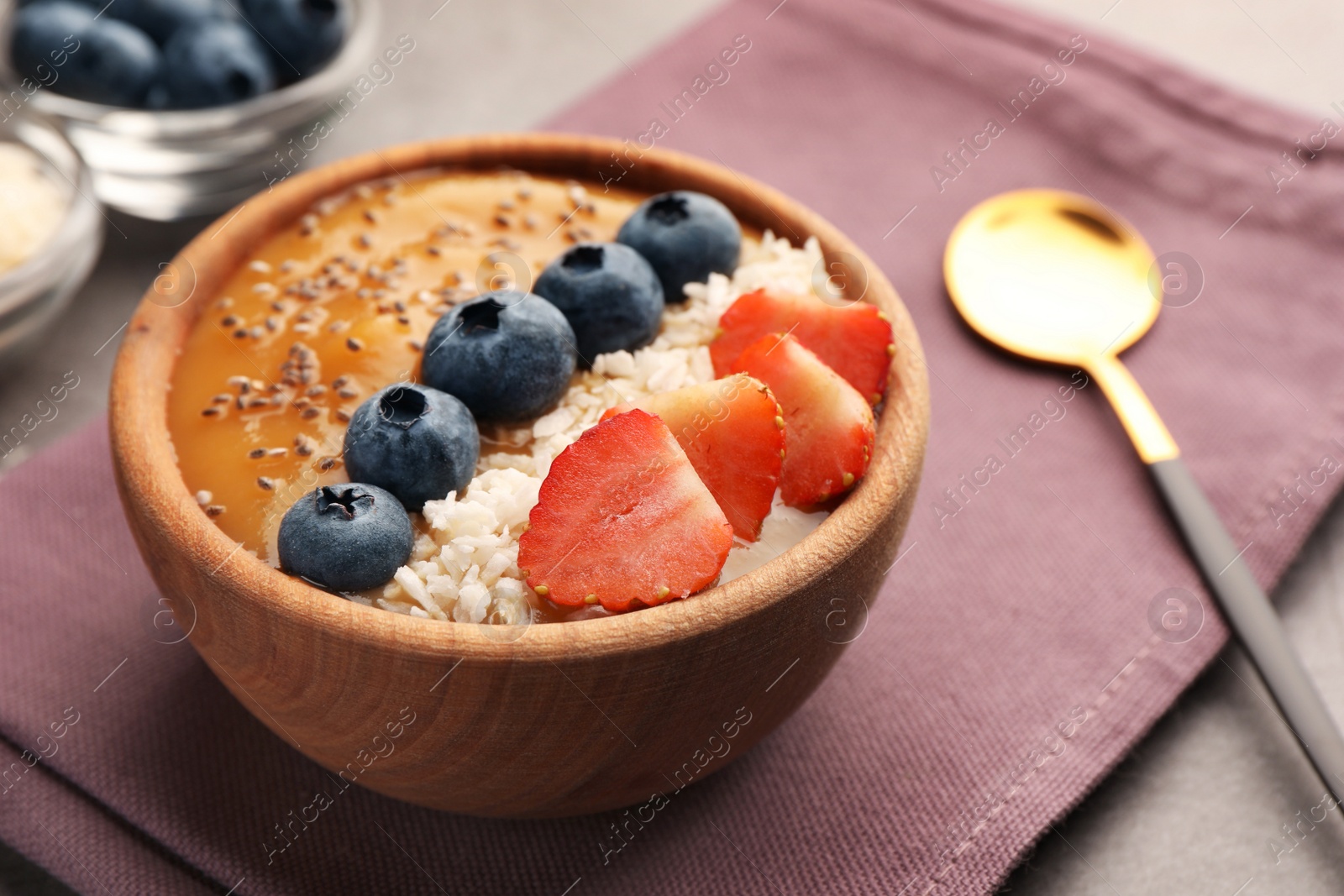 Photo of Delicious smoothie bowl with fresh berries, chia seeds and coconut flakes on grey table, closeup