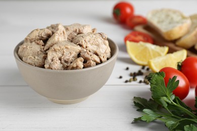 Bowl of tasty cod liver and different products on white wooden table, closeup