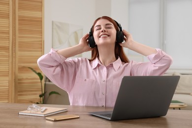 Happy woman with headphones listening to music and laptop on wooden table