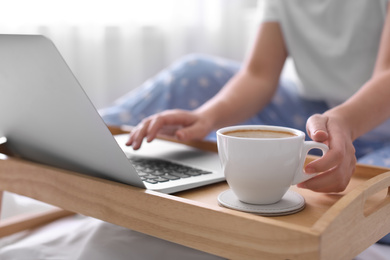 Photo of Woman taking cup of morning coffee while working on laptop indoors, closeup