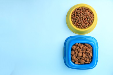 Photo of Dry pet food in feeding bowls on light blue background, flat lay. Space for text