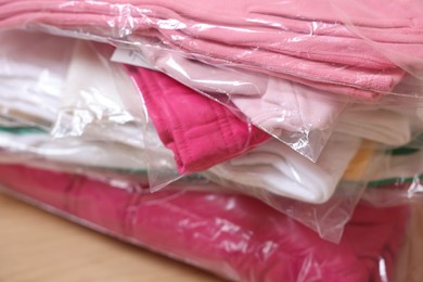Photo of Stack of folded clothes in plastic bags on table, closeup