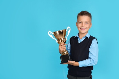 Happy boy in school uniform with golden winning cup on blue background. Space for text