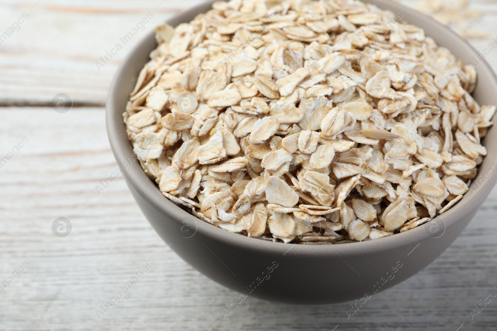 Photo of Bowl of oatmeal on white wooden table, closeup