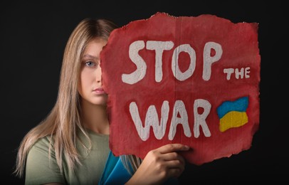 Photo of Sad woman holding poster with words Stop the War on black background