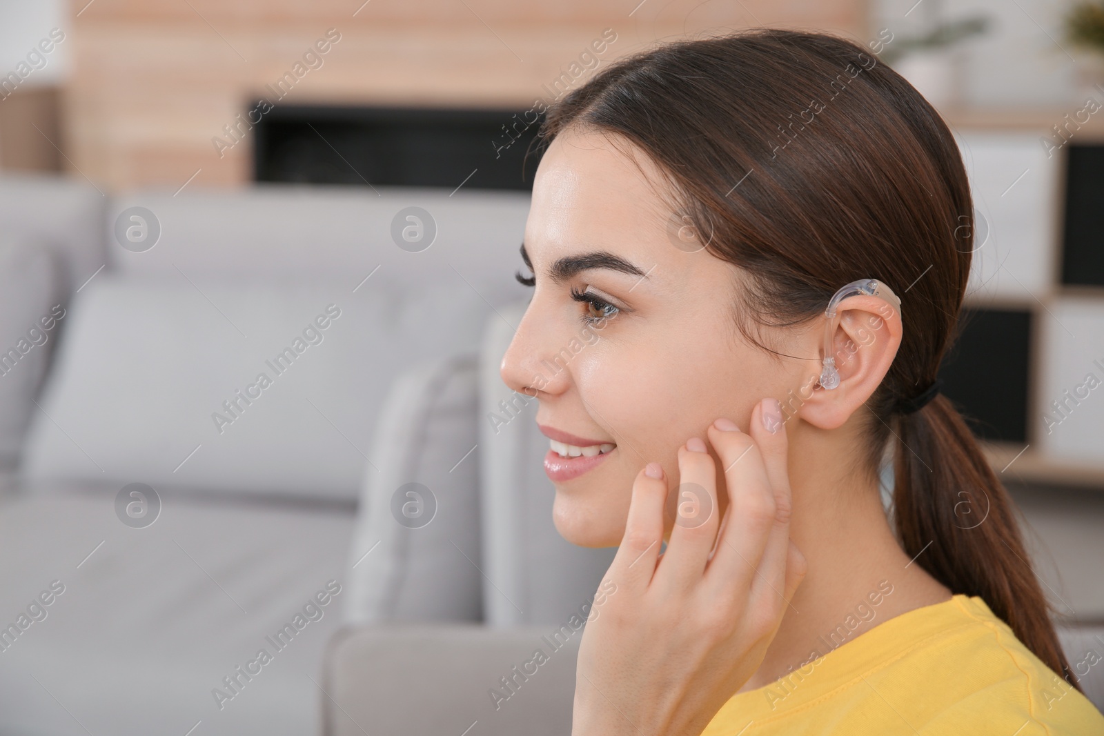 Photo of Young woman with hearing aid indoors. Space for text