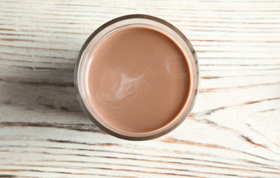 Photo of Glass of tasty chocolate milk on wooden background, top view. Dairy drink