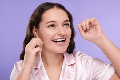 Woman with braces cleaning teeth using dental floss on violet background