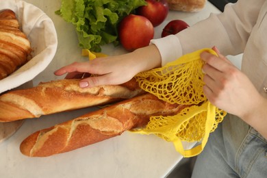 Photo of Woman taking baguettes out from string bag at countertop, closeup