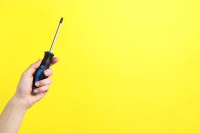 Photo of Woman holding screwdriver on yellow background, closeup. Space for text