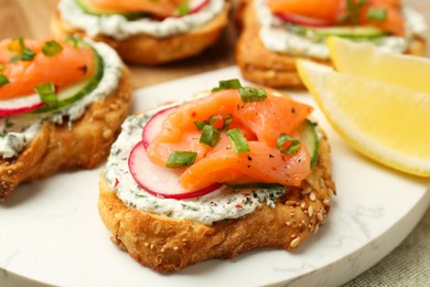 Tasty canapes with salmon, cucumber, radish and cream cheese on table, closeup