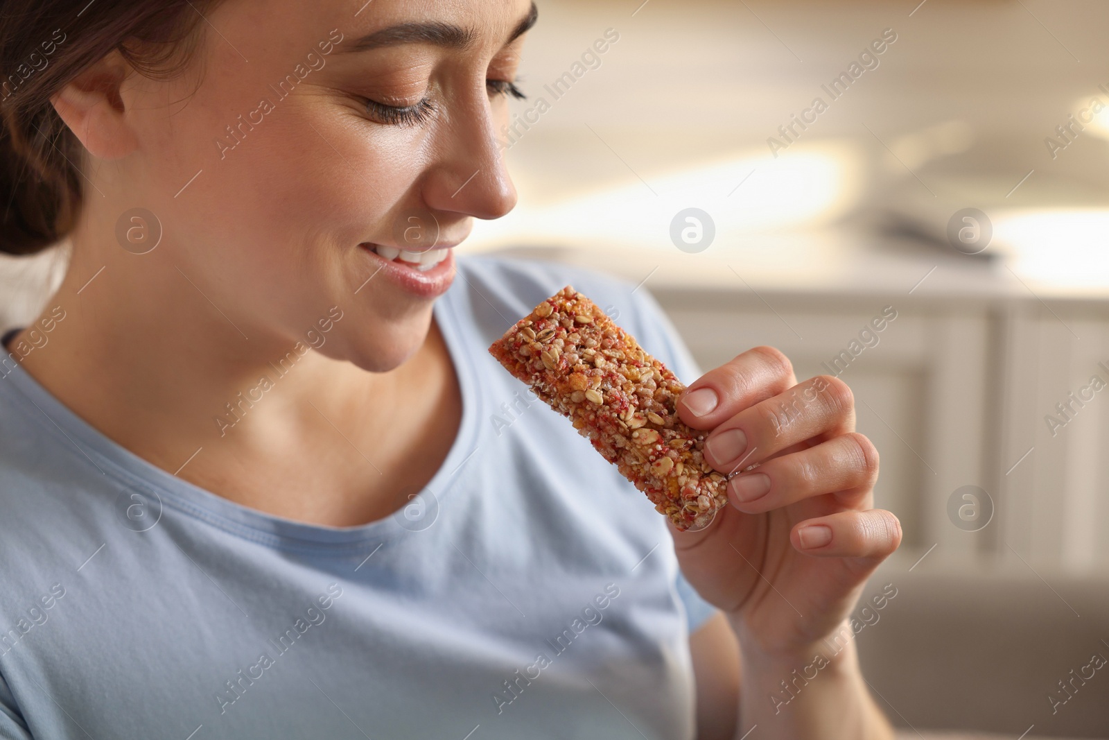 Photo of Woman eating tasty granola bar at home, closeup