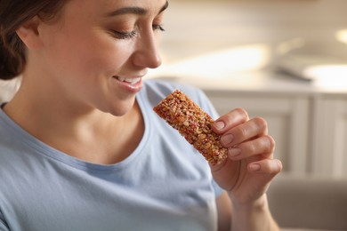 Woman eating tasty granola bar at home, closeup