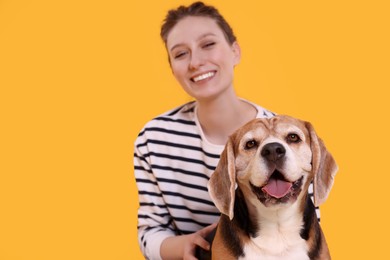 Photo of Happy young woman with cute Beagle dog on orange background, selective focus. Lovely pet